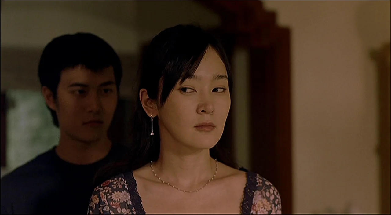 3-Iron (2004) movie still: medium — An interior space features a woman in the foreground and a man behind her. The woman looks away while the man is…