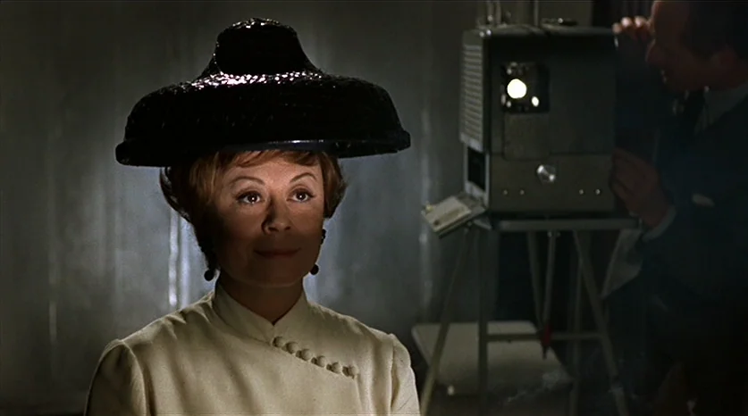 Juliet of the Spirits (1965) movie still: closeup — A dark screening room features a woman positioned in front of a film projector. The woman in a…