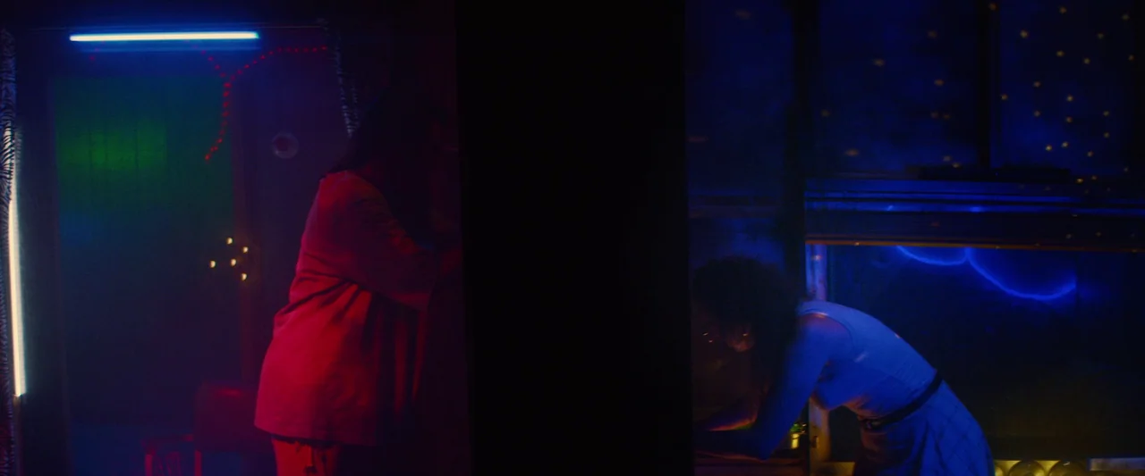 Revealer (2022) movie still: medium — A dark space is divided by a solid black vertical pillar, separating two figures. One woman stands on the left…