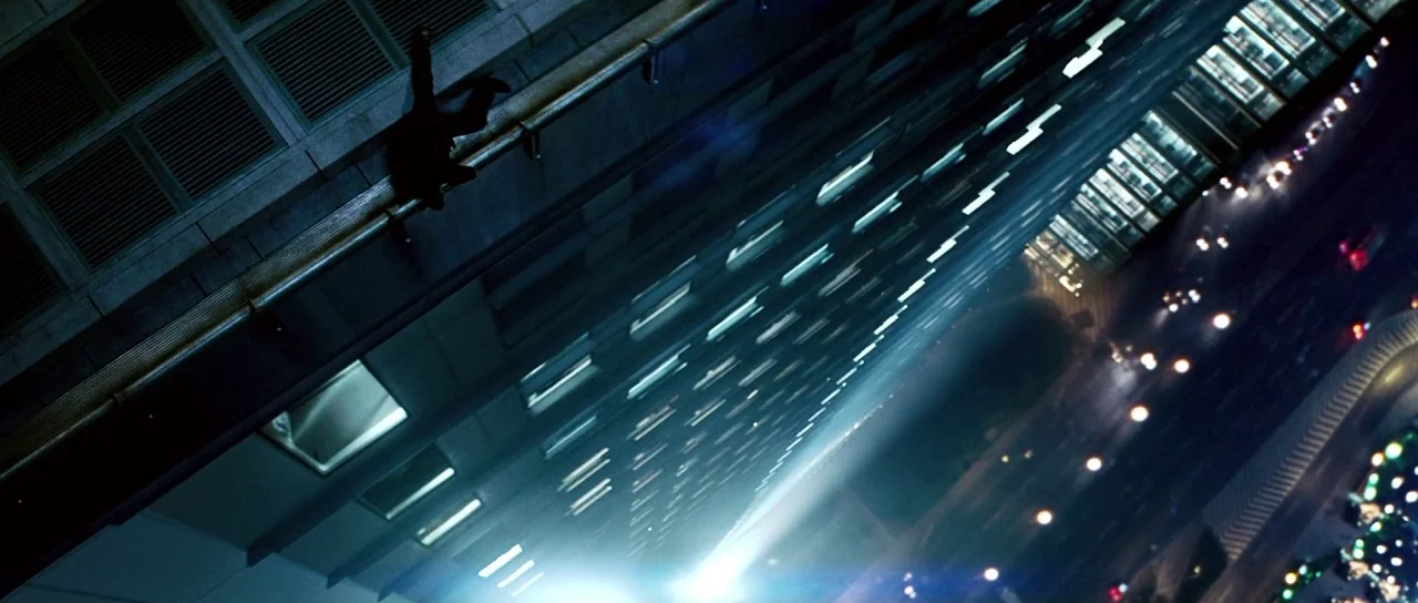Mission: Impossible III (2006) movie still: wide — A vertical perspective showing a dark skyscraper ledge high above a lit city street. A single…