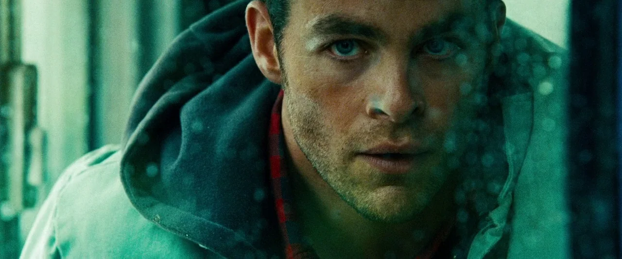 Unstoppable (2010) movie still: closeup — A man peers through a rain-streaked window inside a dimly lit vehicle cabin. The man stares forward with a…