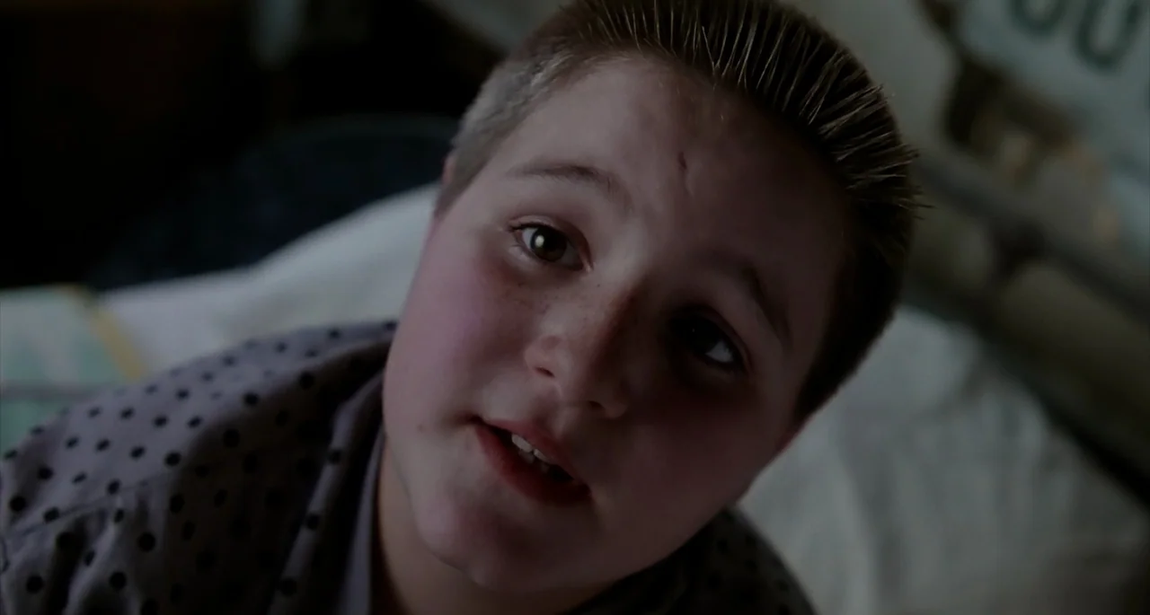 The Addams Family (1991) movie still: closeup — A dark, dimly lit bedroom provides the setting for a child lying in bed. The boy rests on his back…