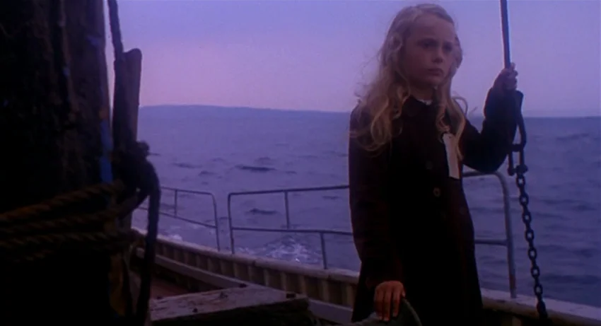 The Secret Of Roan Inish (1994) movie still: medium — A young girl stands on the deck of a boat moving across open water. The sky is dark blue and…