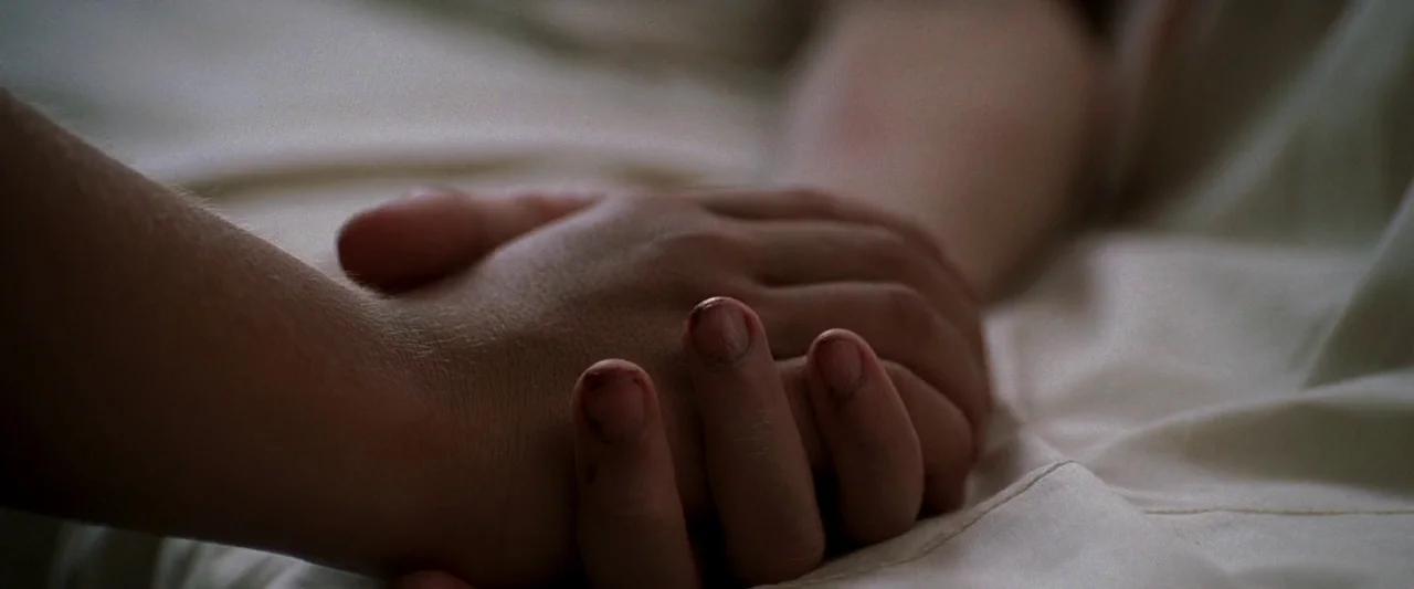 Walk The Line (2005) movie still: closeup — A close view of two hands joined together atop white fabric sheets. One hand rests on top of the other.