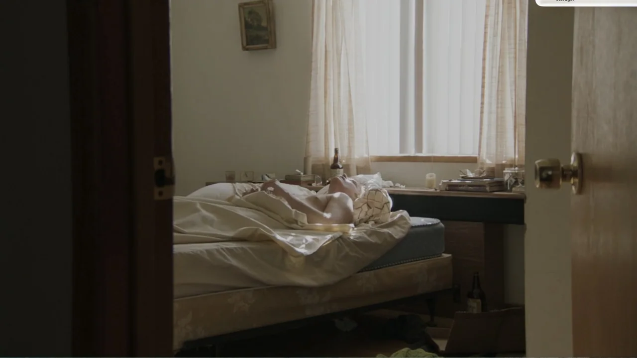 Don't Worry, He Won't Get Far on Foot (2018) movie still: medium — A plain bedroom with a bare mattress, a window with sheer curtains, and glass…