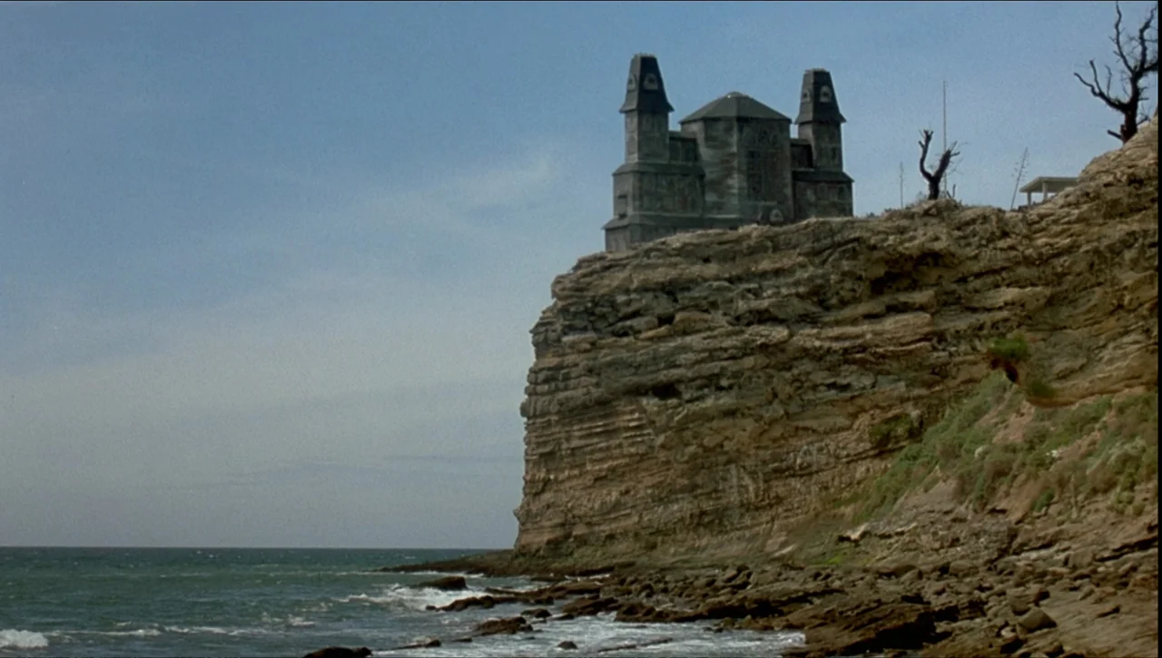 Necronomicon: Book of Dead (1993) movie still: establishing — A gothic-style stone structure sits prominently atop a rugged, layered rock cliff…