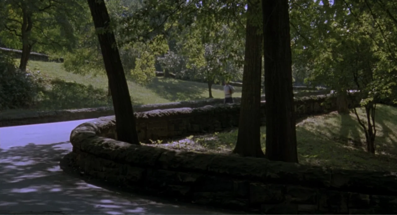 An Experiment in Fear: The Making of Monkey Shines (2014) movie still: wide — A park pathway winds past a low, curved stacked-stone wall beneath…
