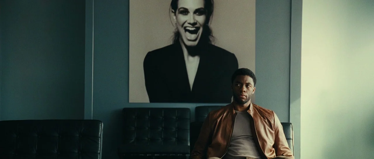 Message From The King (2016) movie still: medium — A waiting room with dark blue walls and black tufted leather chairs. A large black-and-white…