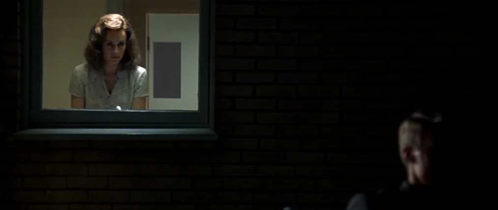 The Insider (1999) movie still: medium — A woman stands behind a window in a dark exterior wall made of bricks. A shadowed man is positioned in the…