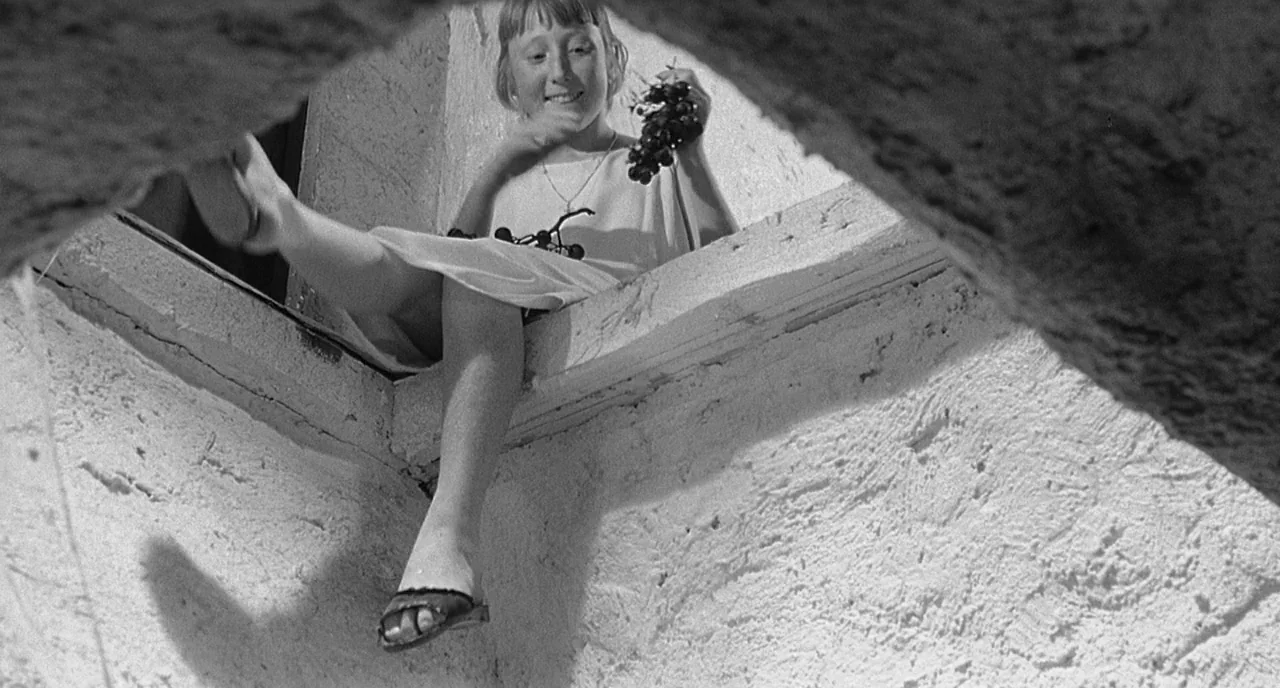 8 1/2 (1963) movie still: medium — A girl sits on a rough stone ledge above the frame with sunlight overhead. She holds a cluster of grapes in her…