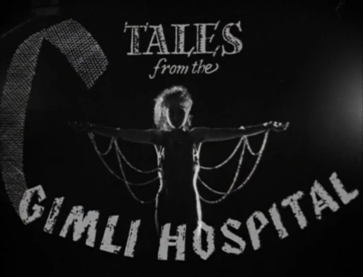 Tales from the Gimli Hospital (1988) movie still: medium — A dark stage features a title graphic floating in front of a woman. She stands centered…