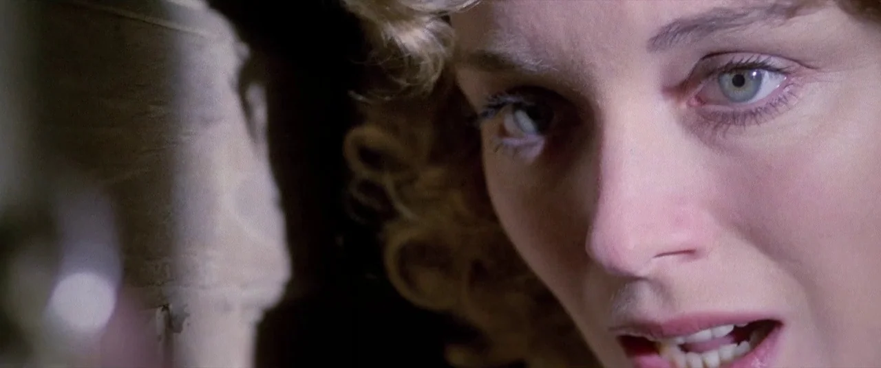 House By The Cemetery (1981) movie still: closeup — A woman's face is framed in a tight close-up against a dark textured background. She looks…