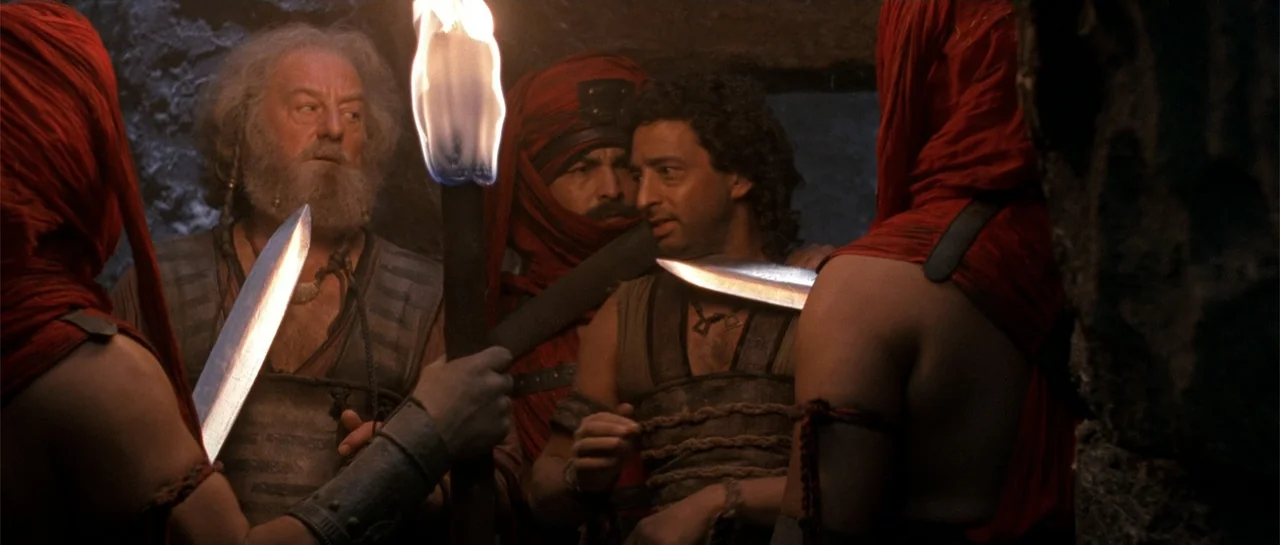 The Scorpion King (2002) movie still: medium — A dark cave interior is illuminated by the flickering light of a handheld torch. Several men in red…