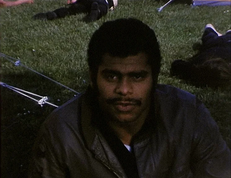 The Niklashausen Journey (1970) movie still: medium — A group of people lies on a grassy area in an outdoor park setting. One man sits in the…