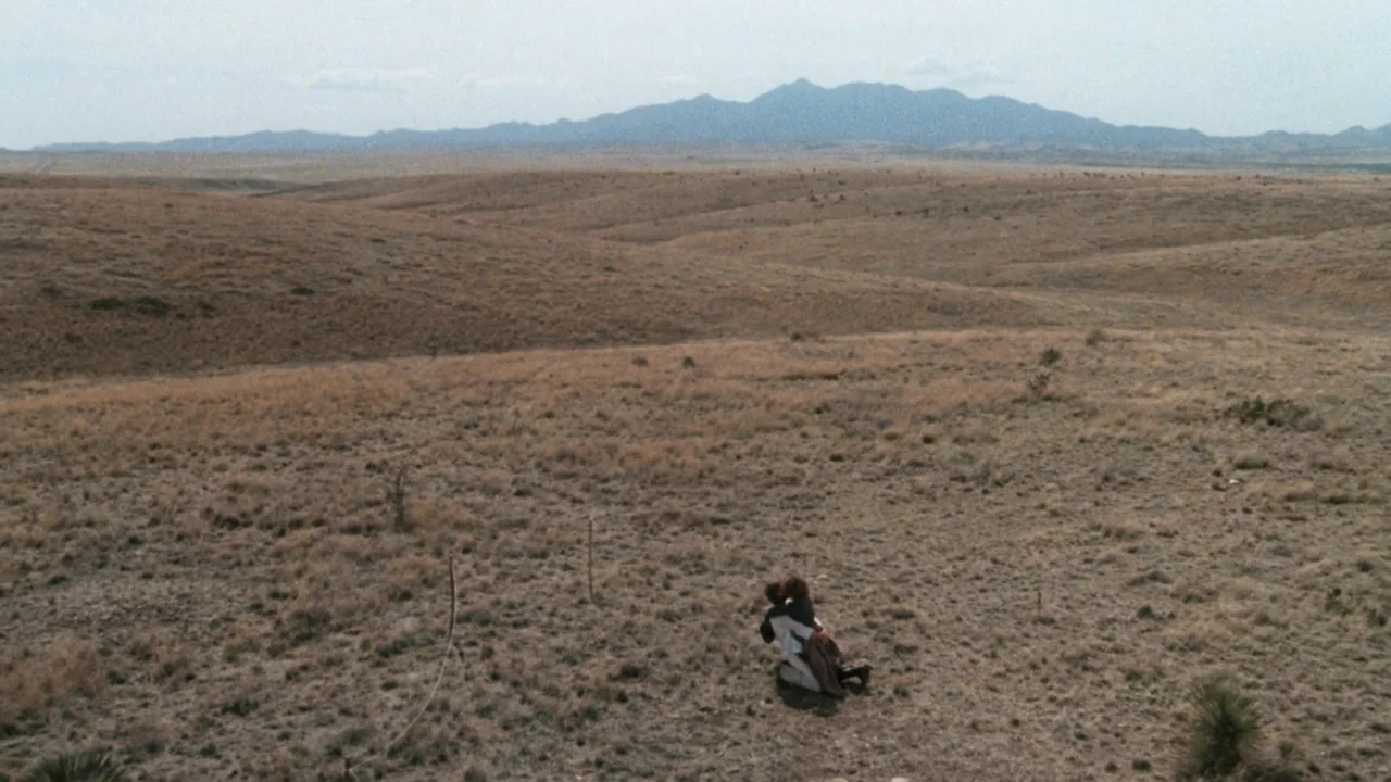 A Star Is Born (1976) movie still: wide — A vast, arid desert plain stretches toward a distant range of low rolling mountains. Two figures kneel…