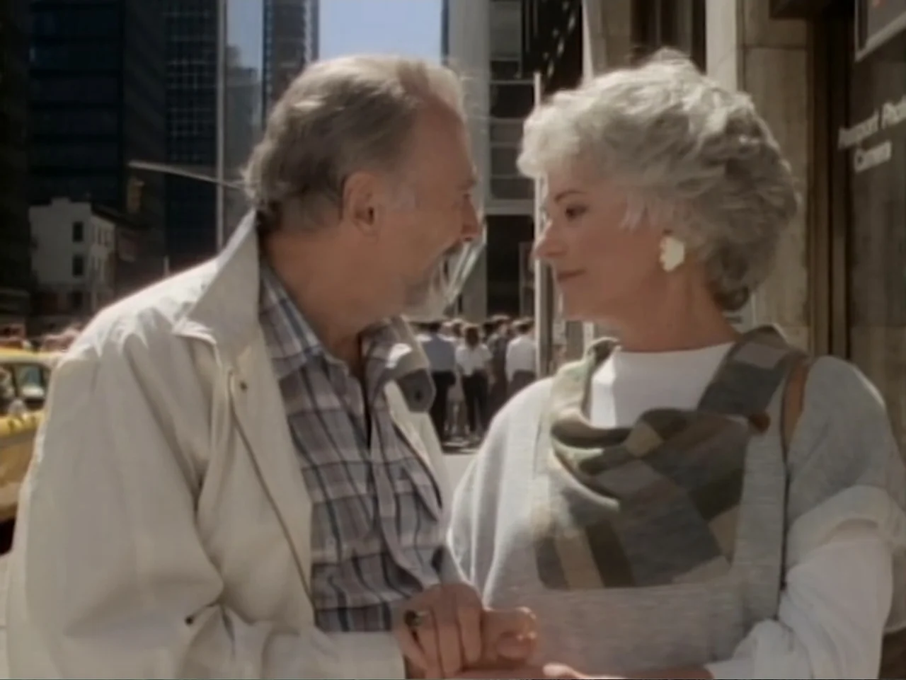 My First Love (1988) movie still: medium — A bustling city sidewalk features skyscrapers and pedestrians in the blurred background. An elderly man…