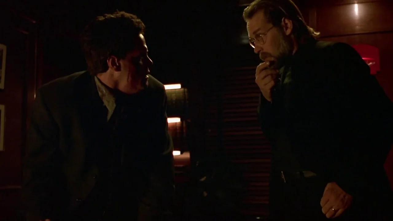 Hellraiser: Inferno (2000) movie still: medium — A dimly lit room with dark wooden wall paneling and horizontal slatted blinds. Two men in suits…