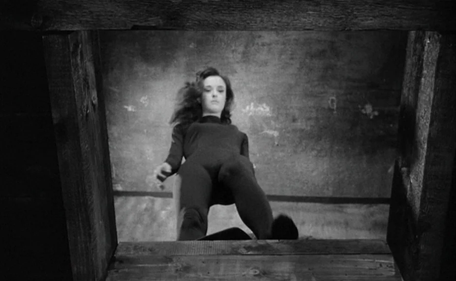 Judex (1966) movie still: fullbody — A dark wooden frame surrounds a view of a person standing above the camera. The background wall is textured and…