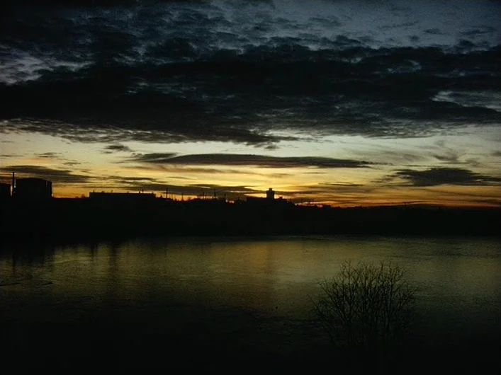 The Death of Maria Malibran (1972) movie still: establishing — A dark river reflects the golden-yellow light of a sunset behind a distant skyline.…