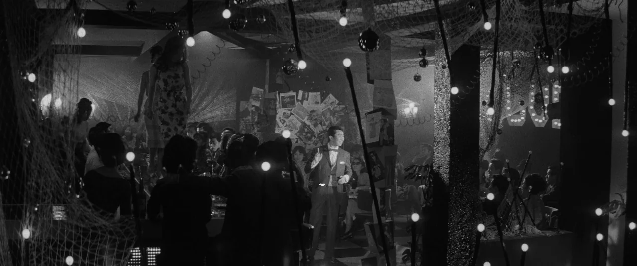 Carmen From Kawachi (1966) movie still: wide — A dark, densely populated nightclub space decorated with string lights and hanging nets. The patrons…