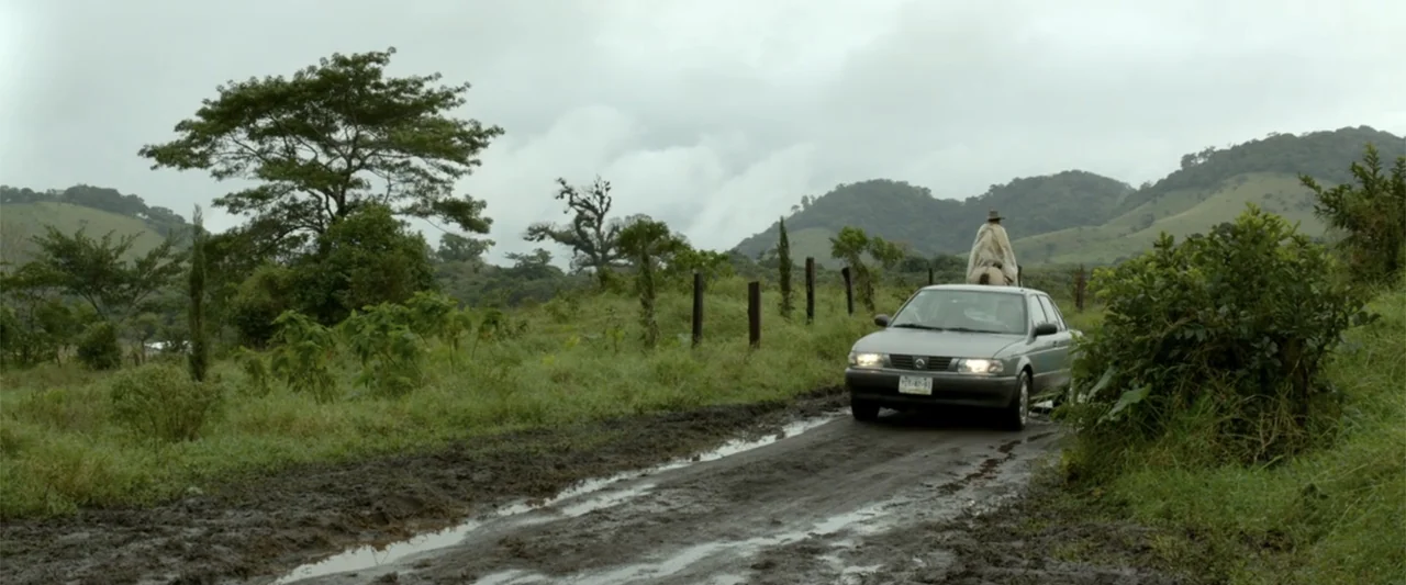 I Dream in Another Language (2017) movie still: wide — A muddy rural track winds through a green hilly landscape under a clouded sky. A lone rider…