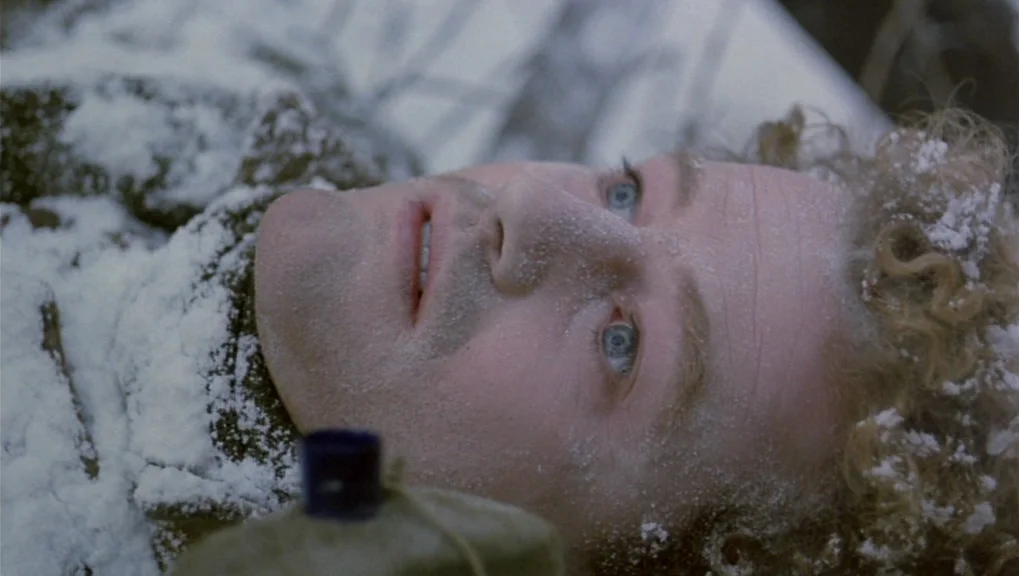 War Requiem (1989) movie still: closeup — A man lies on his back on ground covered in fresh white snow. The man's face and curly hair are dusted…