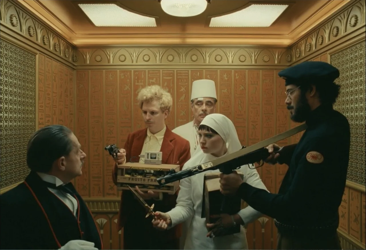 The Phoenician Scheme (2025) movie still: medium — The interior of an elevator with embossed golden wall panels featuring Egyptian motifs. Four…