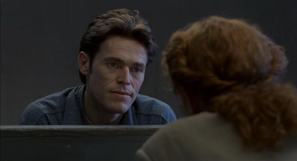 Light Sleeper (1992) movie still: medium — A spartan room features a solid grey wall and a gray partition divider. A man sits opposite a person seen…
