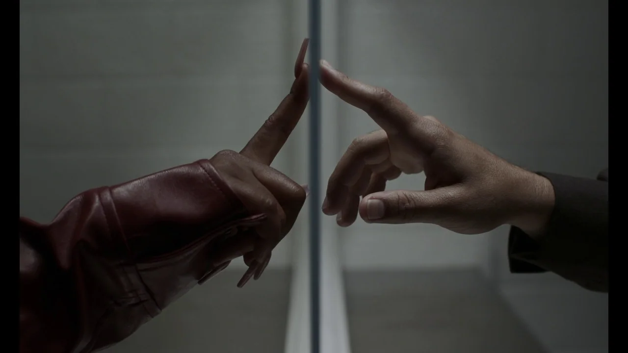 The Card Counter (2021) movie still: closeup — A dimly lit space features a reflective surface bisecting the frame vertically. One hand with long…