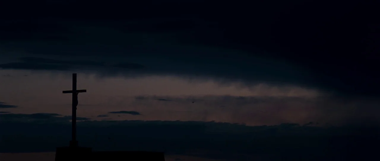 Our Day Will Come (2010) movie still: establishing — A silhouette of a crucifix sits atop a building against a dark night sky. Clouds stretch across…