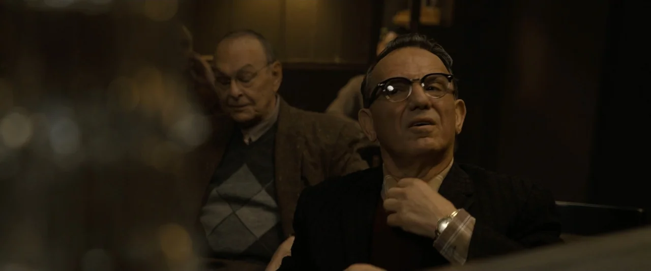 The Alto Knights (2025) movie still: medium — A dimly lit interior space features two elderly men sitting together at a table. The man in the…