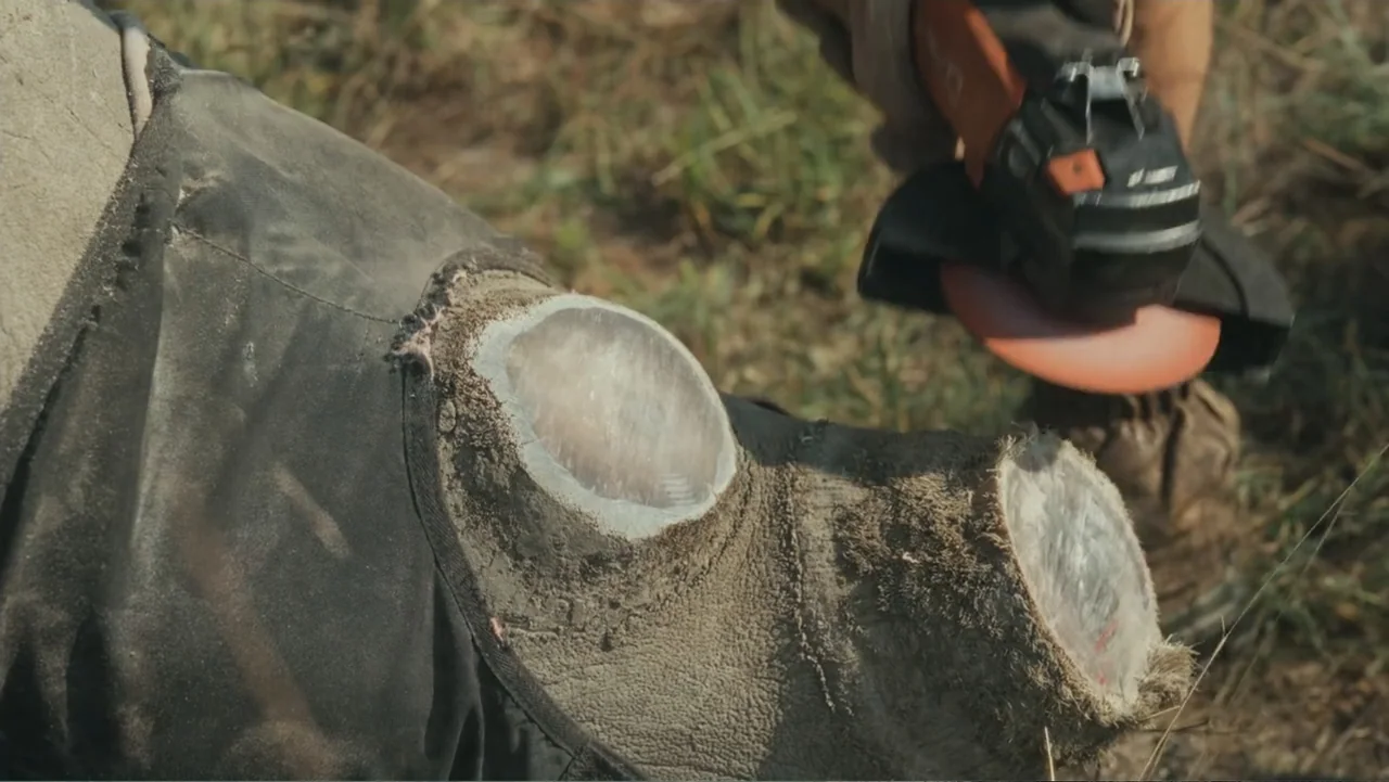 Bloody Trophy (2025) movie still: closeup — A grassy field surface provides the backdrop for a close industrial cutting task. An angle grinder…