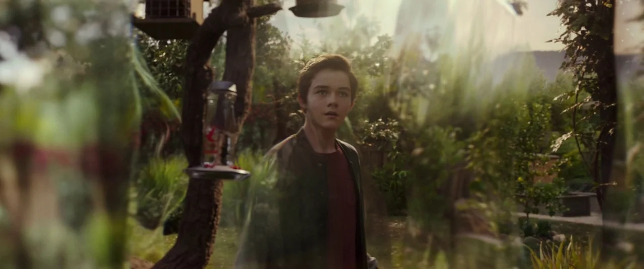 A Wrinkle In Time (2018) movie still: medium — A sunny residential backyard features leafy trees and a bird feeder hanging nearby. A teenage boy…