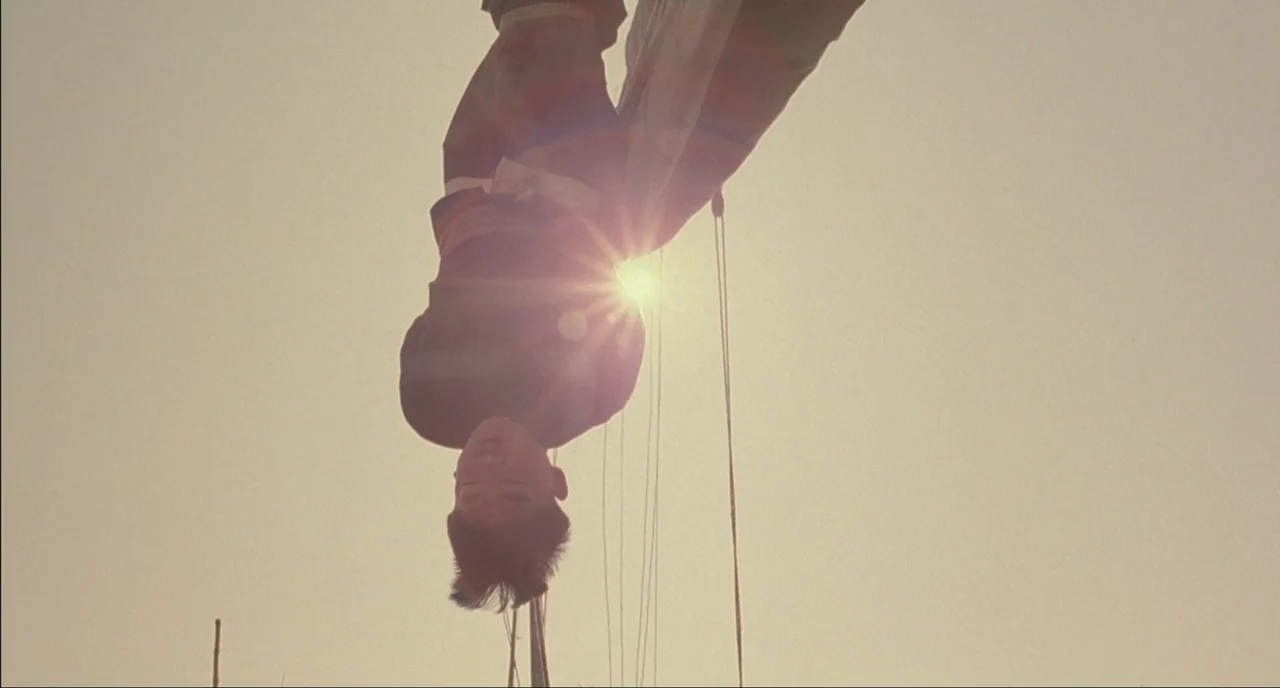 Shanghai Triad (1995) movie still: medium — A person hangs suspended upside down against a bright, clear, golden sky. The sun is positioned directly…