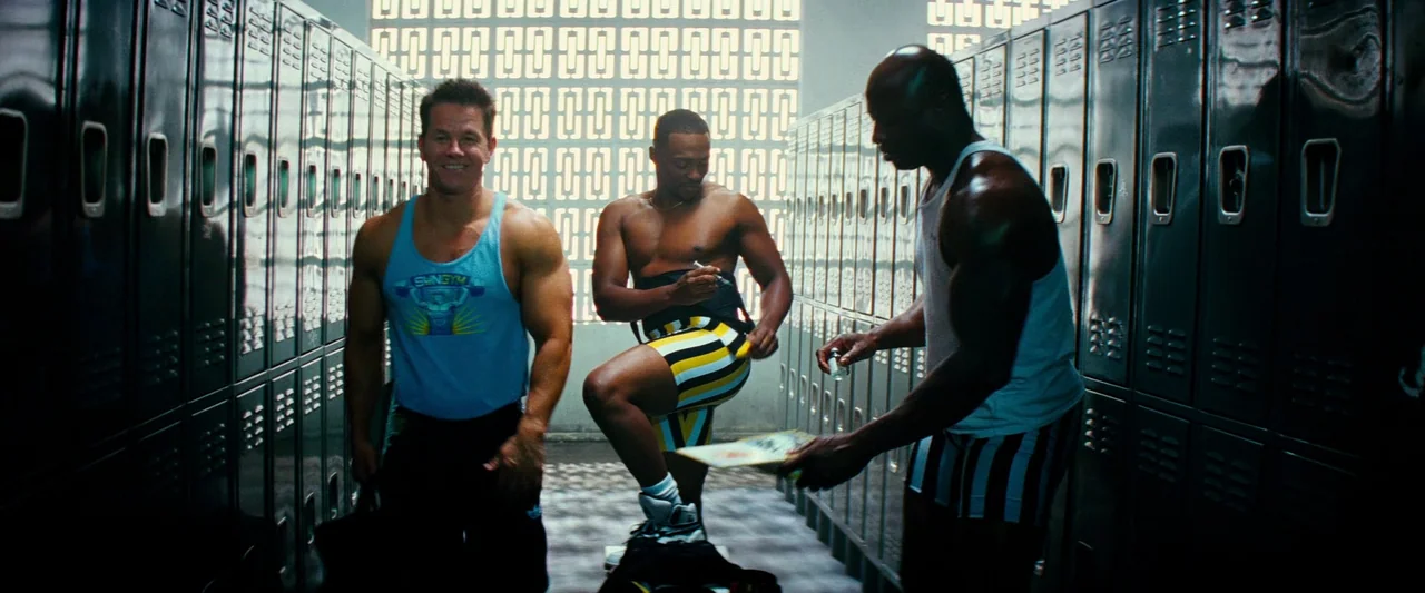 Pain & Gain (2013) movie still: fullbody — A locker room with metallic grey lockers lining walls and patterned concrete block windows. Three…