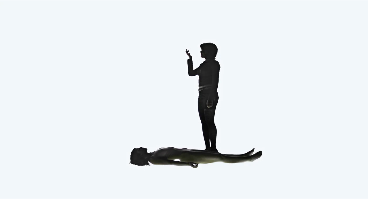 Under The Skin (2013) movie still: wide — An abstract, high-key white void contains two figures in silhouette. One woman stands while the other…