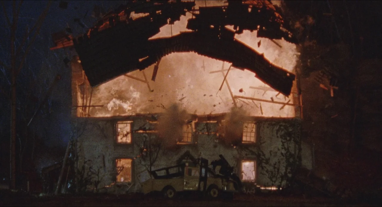 Dog Soldiers (2002) movie still: wide — A two-story stone house at night is consumed by a violent explosion and flames. The roof of the building…