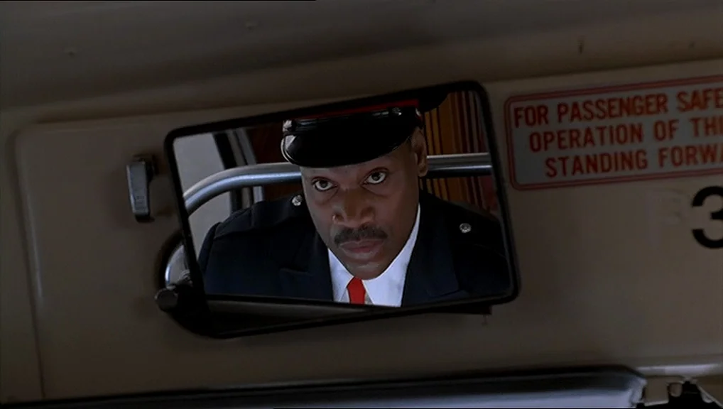 The Truman Show movie still: closeup — The interior of a city bus features a cream-colored ceiling and a warning sign. A bus driver is visible…