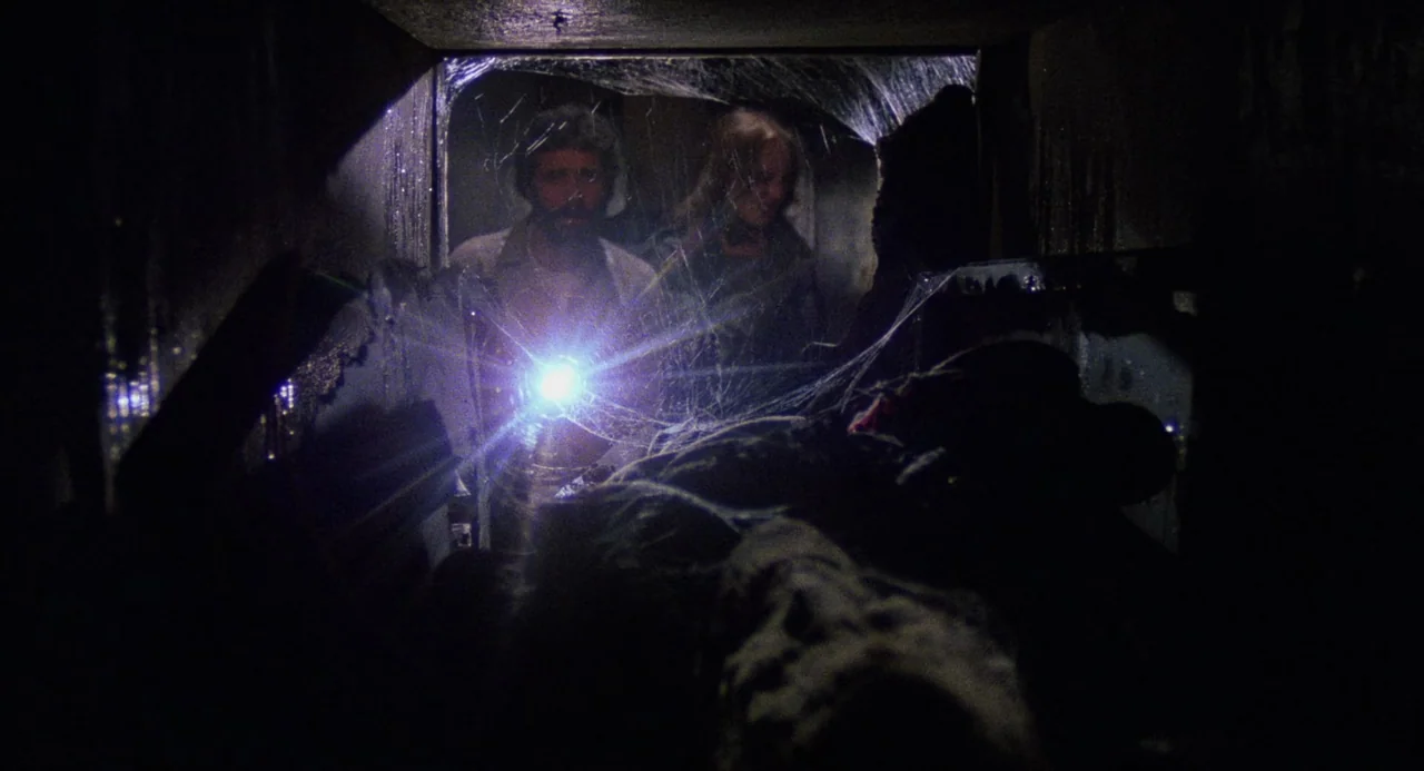 City of the Living Dead (1980) movie still: medium — A claustrophobic crawlspace contains thick spiderwebs and dust. Two people with a flashlight…