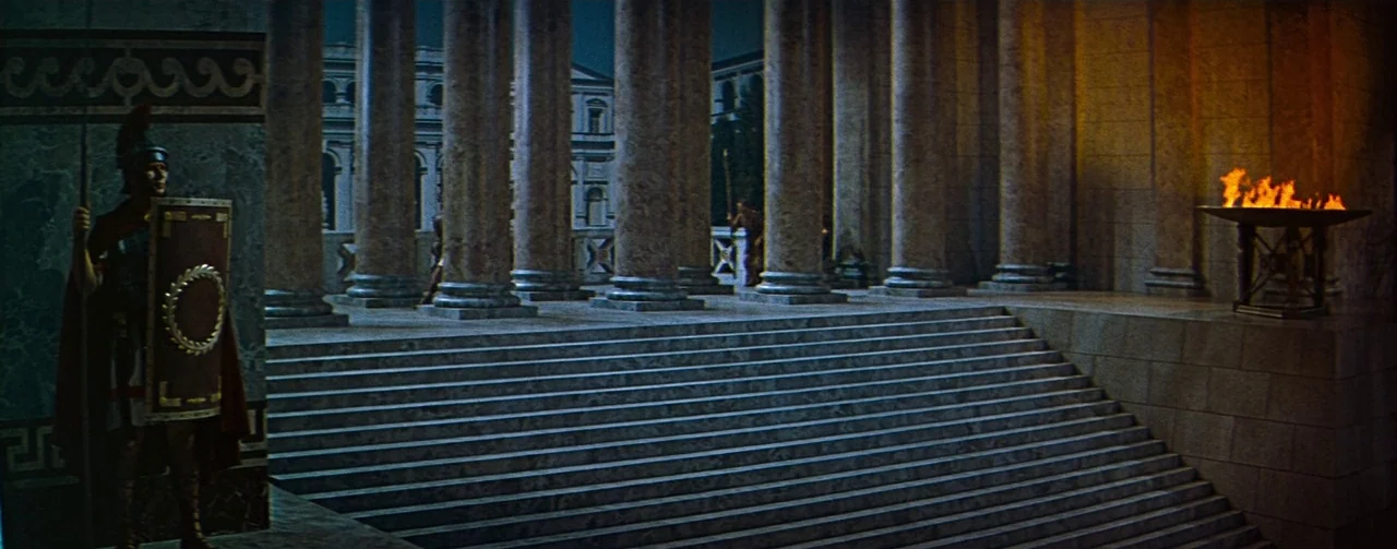 The Robe (1953) movie still: wide — A stone colonnade with a long flight of stairs leads toward an open square. A lone Roman soldier in full armor…