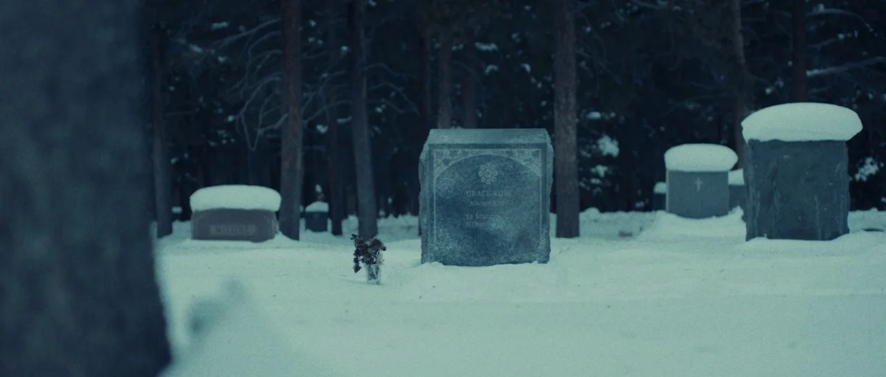Starfish (2018) movie still: wide — A quiet cemetery clearing features rows of headstones covered in thick, fresh snowfall. A single granite marker…