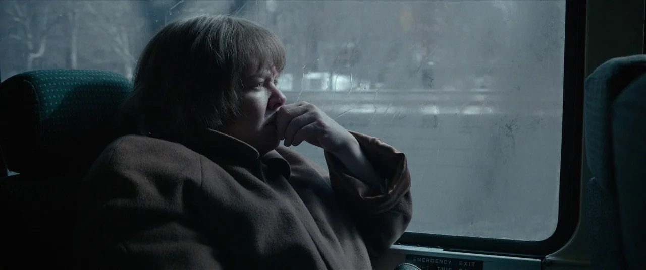 Can You Ever Forgive Me? (2018) movie still: medium — The interior of a passenger bus with green fabric headrests and rain-streaked windows. A woman…