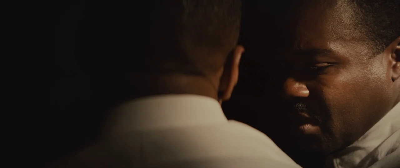 Selma (2014) movie still: closeup — Two men face each other in a dimly lit, nondescript interior space. One man is partially obscured in the…