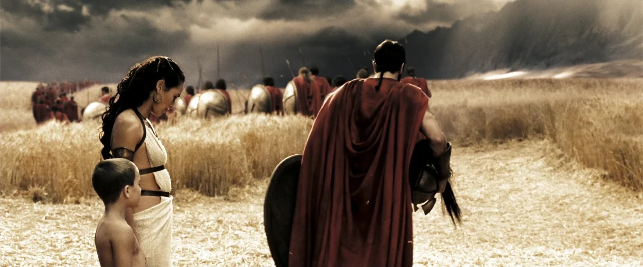 300 (2007) movie still: medium — An open field of golden wheat is populated by soldiers in red cloaks. A woman and a young child stand in the…