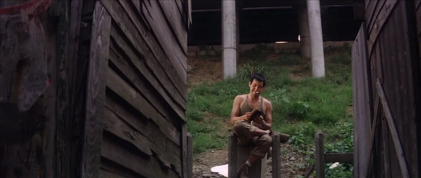 Gate of Flesh (1964) movie still: medium — An outdoor area situated beneath a concrete overpass with weathered wooden structures on both sides. A…