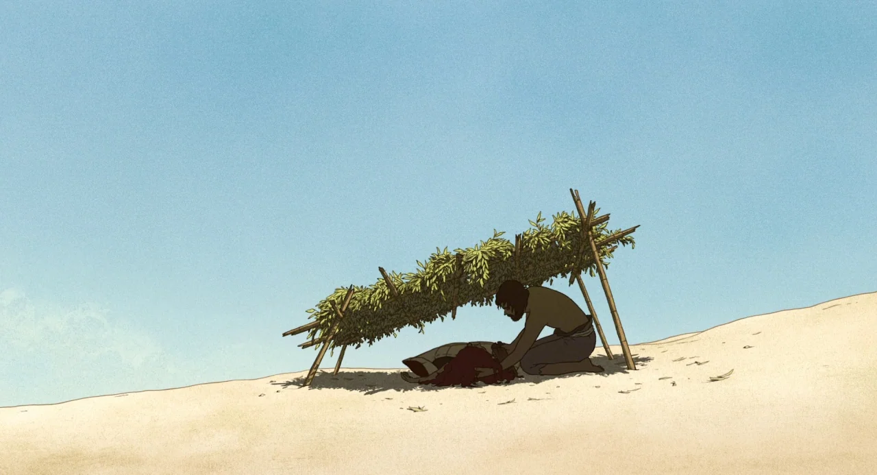 The Red Turtle (2016) movie still: wide — A makeshift shelter built from bamboo sticks and green leaves sits on sand dunes. A man kneels on the…
