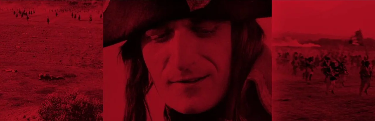 Napoleon (1927) movie still: closeup — A close portrait of a man in a Napoleonic hat against a battlefield backdrop. The man gazes downward while…