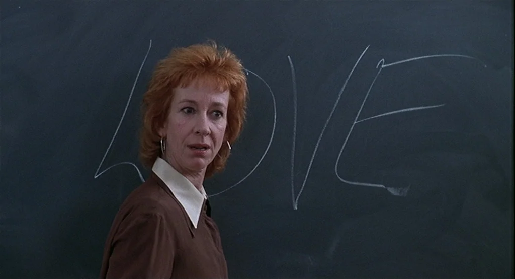 Deux (2002) movie still: medium — A school teacher stands before a large dark chalkboard with the word love written. The woman is positioned…