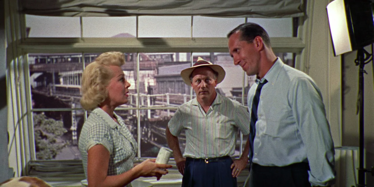 Imitation of Life (1959) movie still: medium — A well-lit room features a large window overlooking an industrial cityscape with elevated tracks. A…