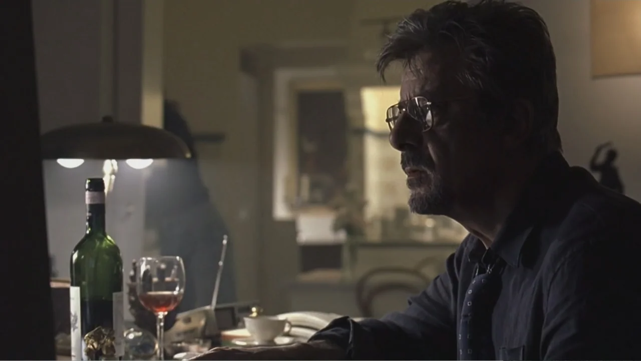 Hannibal (2001) movie still: medium — A dimly lit room contains a desk cluttered with a wine bottle and glass. A man with glasses sits at the desk…